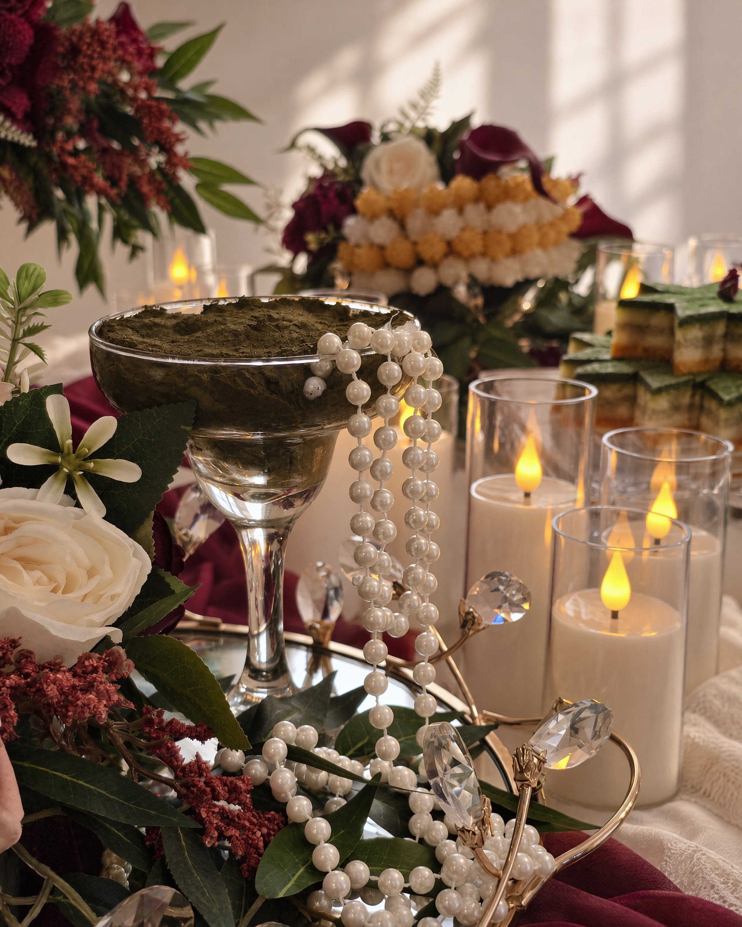 Pearl strands falling over a coupe of henna paste on a mirrored tray, crystal and candles beside it