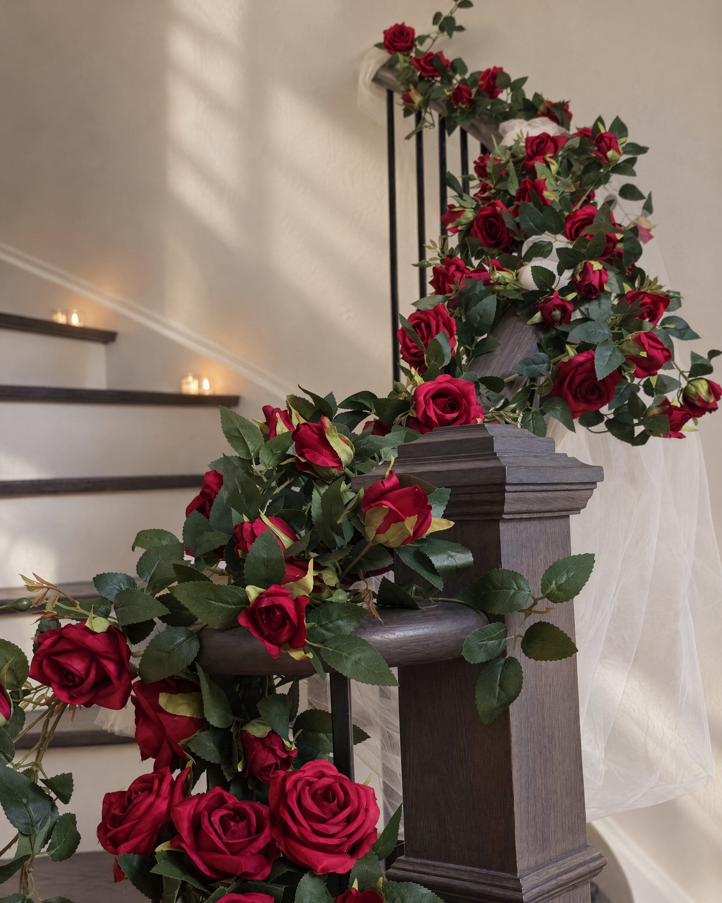 Red roses and eucalyptus spilling over the newel post at the foot of the staircase, a candle on the step behind